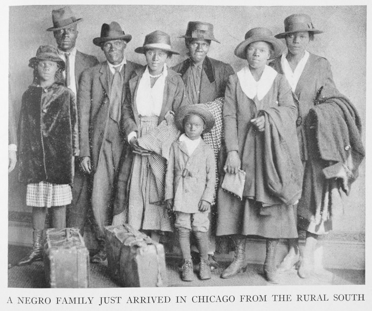 A group of African Americans, six adults and two children, all wearing hats pose with their suitcases